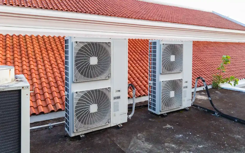 Air conditioning units on a rooftop with a tiled roof in the background.