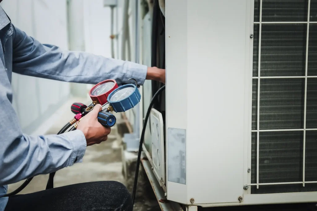 air conditioner technician is using a manifold gauge to check the refrigerant in the system to inspect and repair the outdoor air compressor.